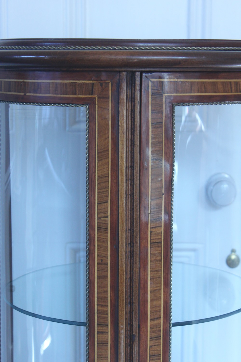 A late 19th-century cylindrical French vitrine cabinet featuring inlaid timber patterning, curved glass panels, tufted red velvet interior lining, and brass claw feet. View XIV