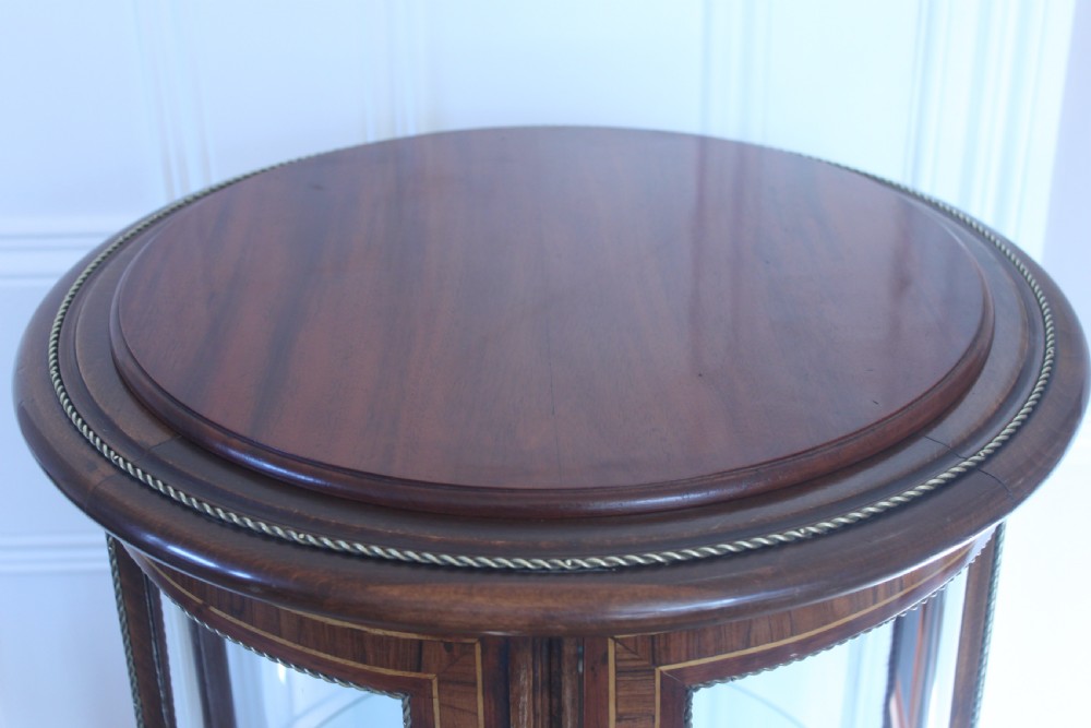 A late 19th-century cylindrical French vitrine cabinet featuring inlaid timber patterning, curved glass panels, tufted red velvet interior lining, and brass claw feet. View XV