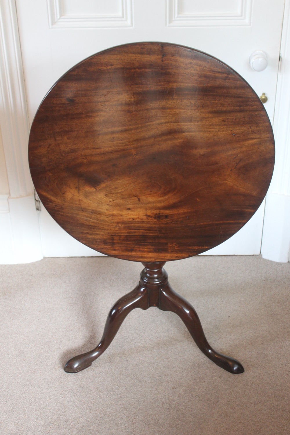 A George III dark mahogany circular tilt-top table displayed upright on a turned central pedestal with three cabriole legs.