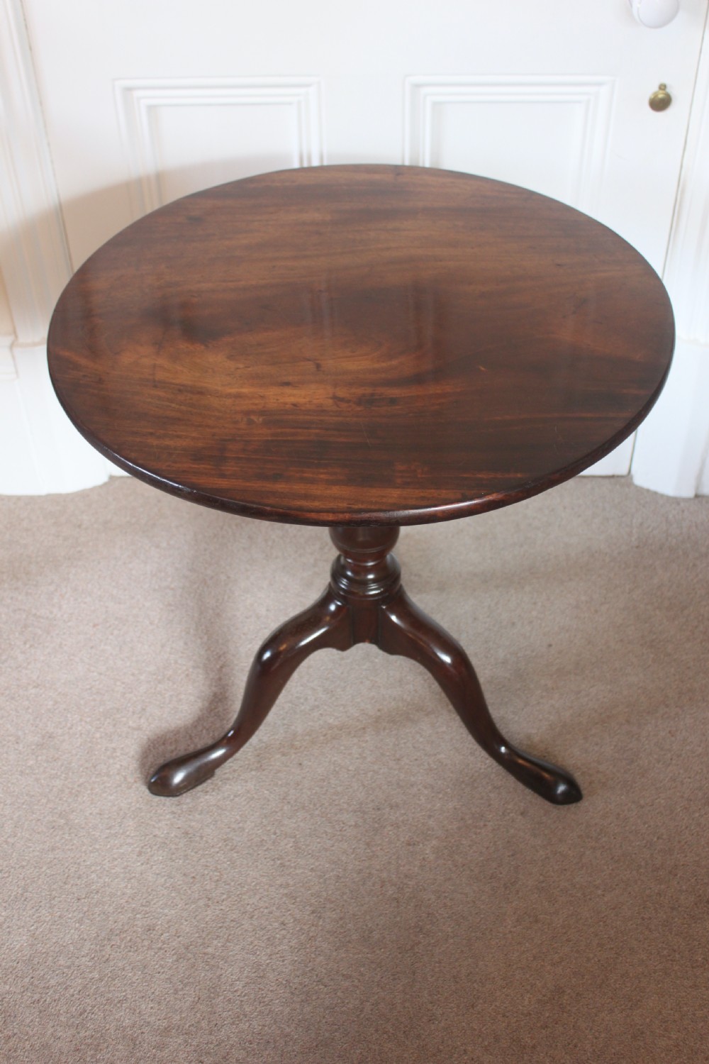 A George III dark mahogany circular tilt-top table displayed upright on a turned central pedestal with three cabriole legs. View II