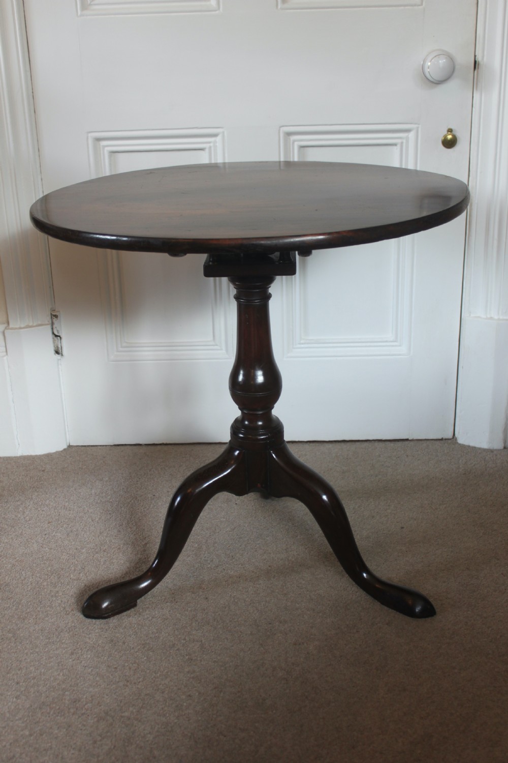 A George III dark mahogany circular tilt-top table displayed upright on a turned central pedestal with three cabriole legs. View III