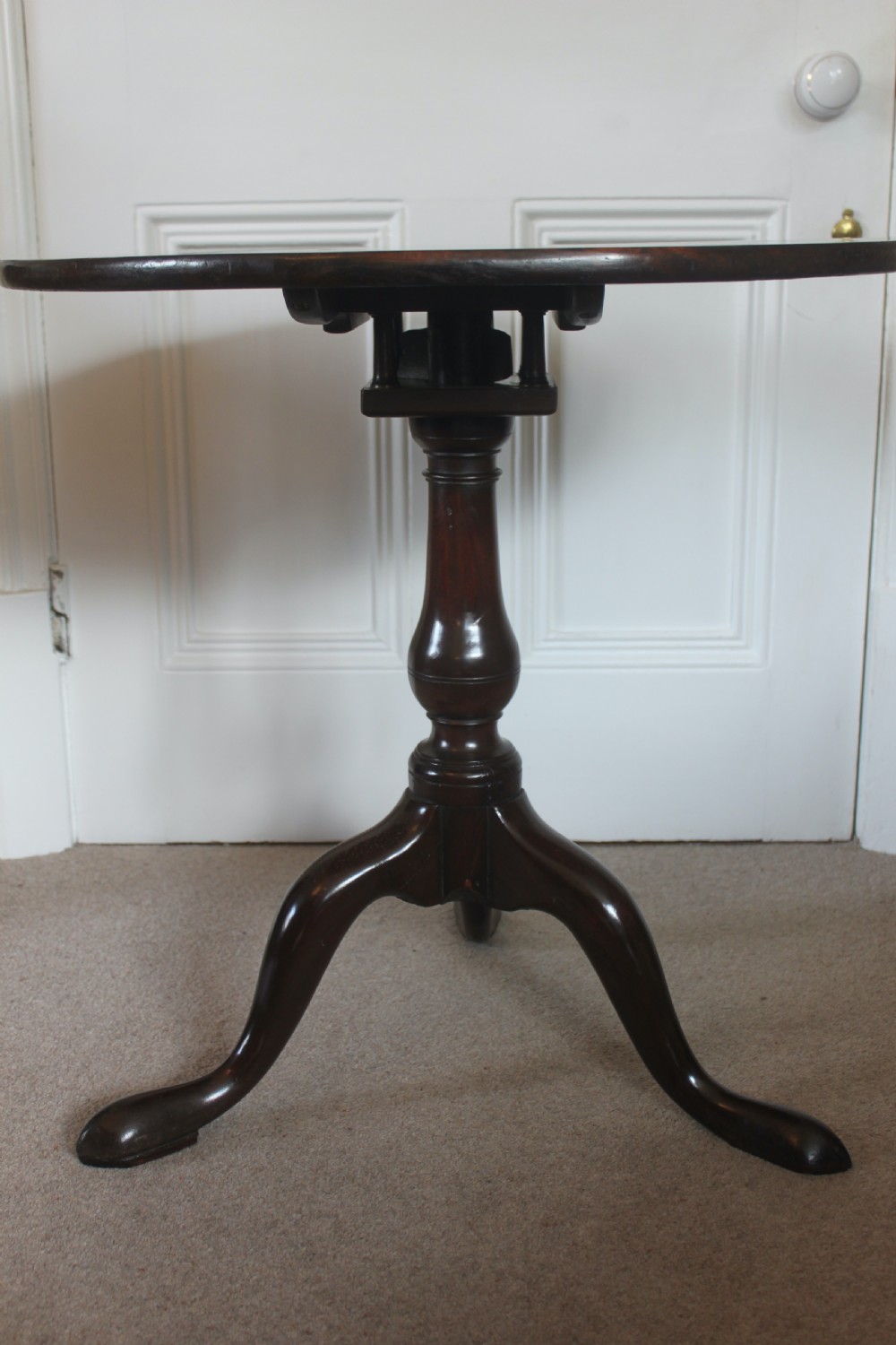 A George III dark mahogany circular tilt-top table displayed upright on a turned central pedestal with three cabriole legs. View V