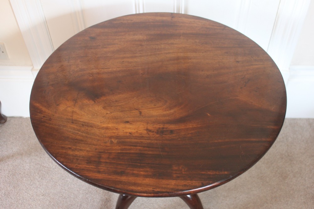 A George III dark mahogany circular tilt-top table displayed upright on a turned central pedestal with three cabriole legs. View VI