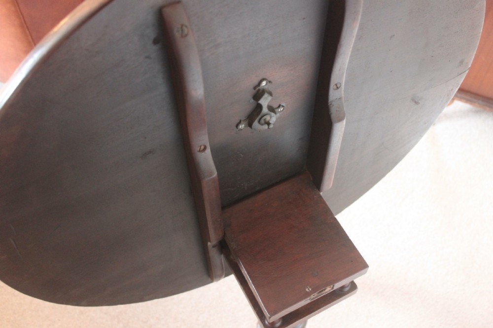A George III dark mahogany circular tilt-top table displayed upright on a turned central pedestal with three cabriole legs. View VII