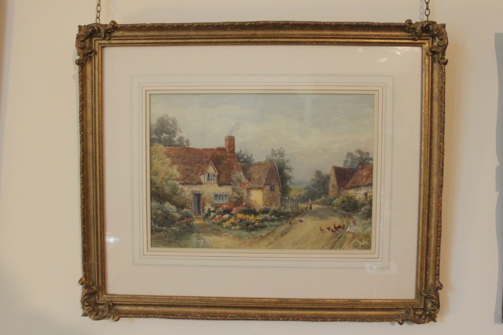 A framed watercolour landscape painting by Harold Lawes depicting a thatched English country cottage along a dirt road with chickens, enclosed in a gilded frame with a cream mount.