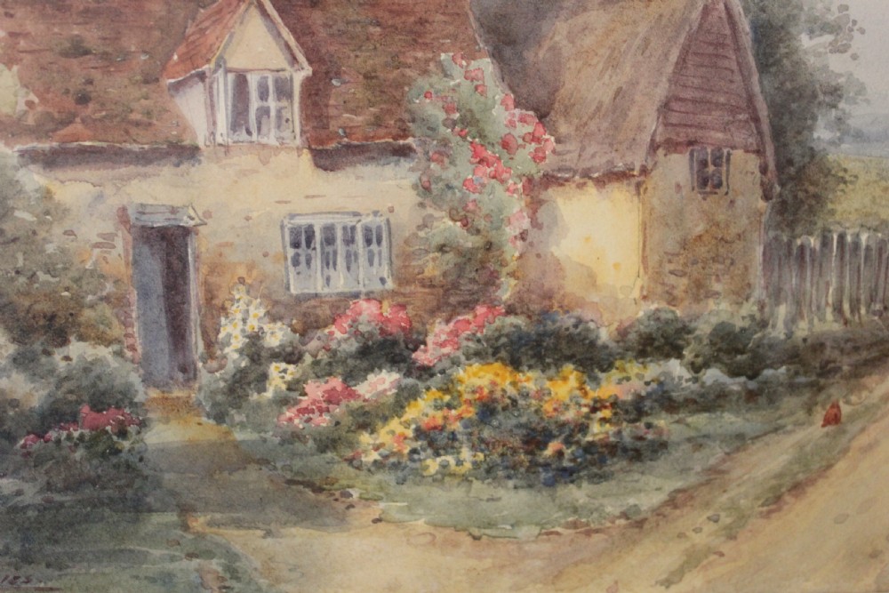 A framed watercolour landscape painting by Harold Lawes depicting a thatched English country cottage along a dirt road with chickens, enclosed in a gilded frame with a cream mount. View V