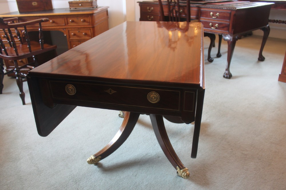 A dark mahogany Regency Pembroke table featuring brass line inlay, a single end drawer, drop leaves, and quadform sabre legs with brass cap castors.