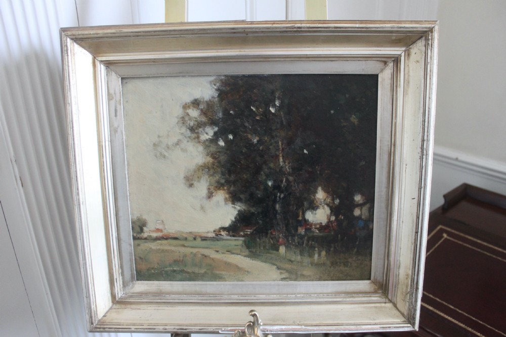 An antique oil painting on wooden panel depicting a muted rural landscape with trees and a track, presented in a wide silver gilt frame. View II