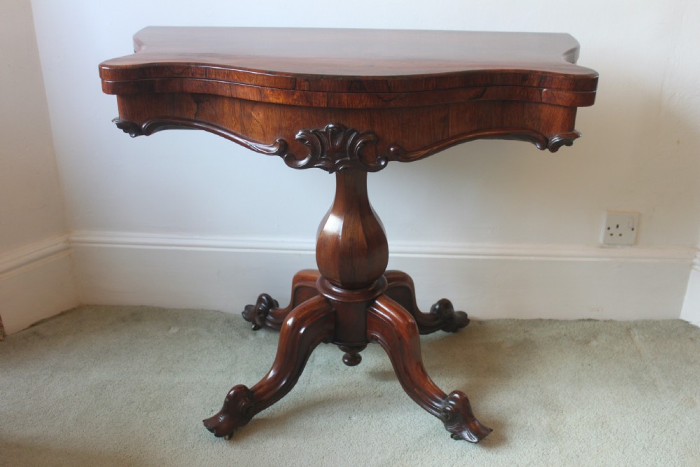A Victorian rosewood foldover tea table featuring a serpentine front, carved pedestal stem, and quad-form cabriole legs.