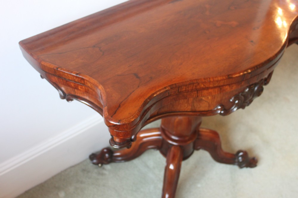 A Victorian rosewood foldover tea table featuring a serpentine front, carved pedestal stem, and quad-form cabriole legs. View V