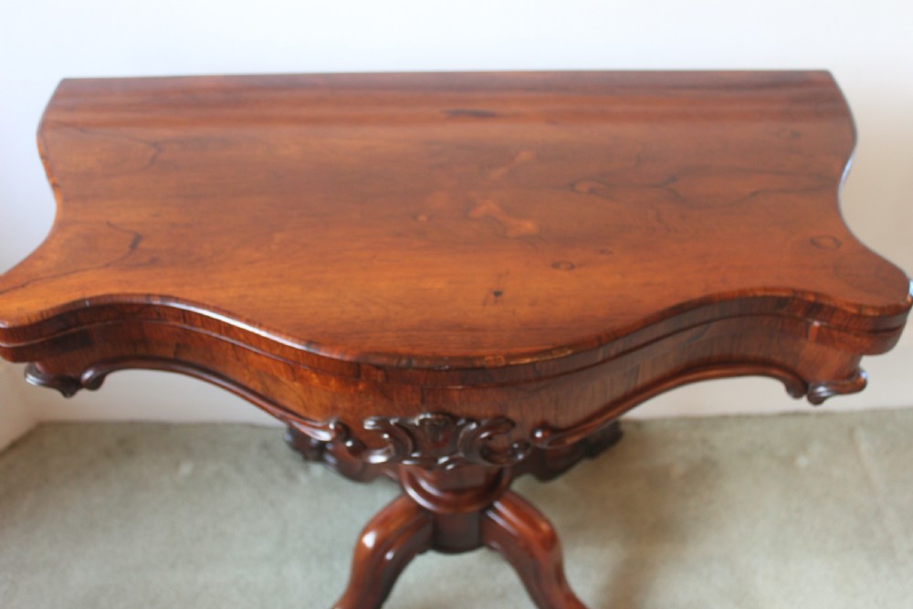 A Victorian rosewood foldover tea table featuring a serpentine front, carved pedestal stem, and quad-form cabriole legs. View XI