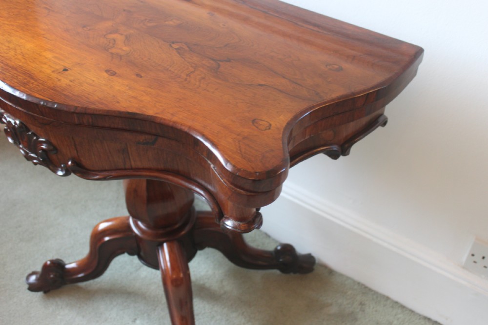 A Victorian rosewood foldover tea table featuring a serpentine front, carved pedestal stem, and quad-form cabriole legs. View XII