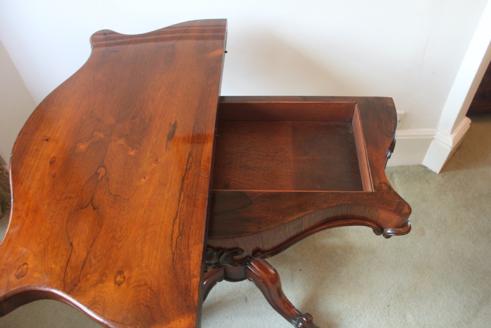 A Victorian rosewood foldover tea table featuring a serpentine front, carved pedestal stem, and quad-form cabriole legs. View XIV