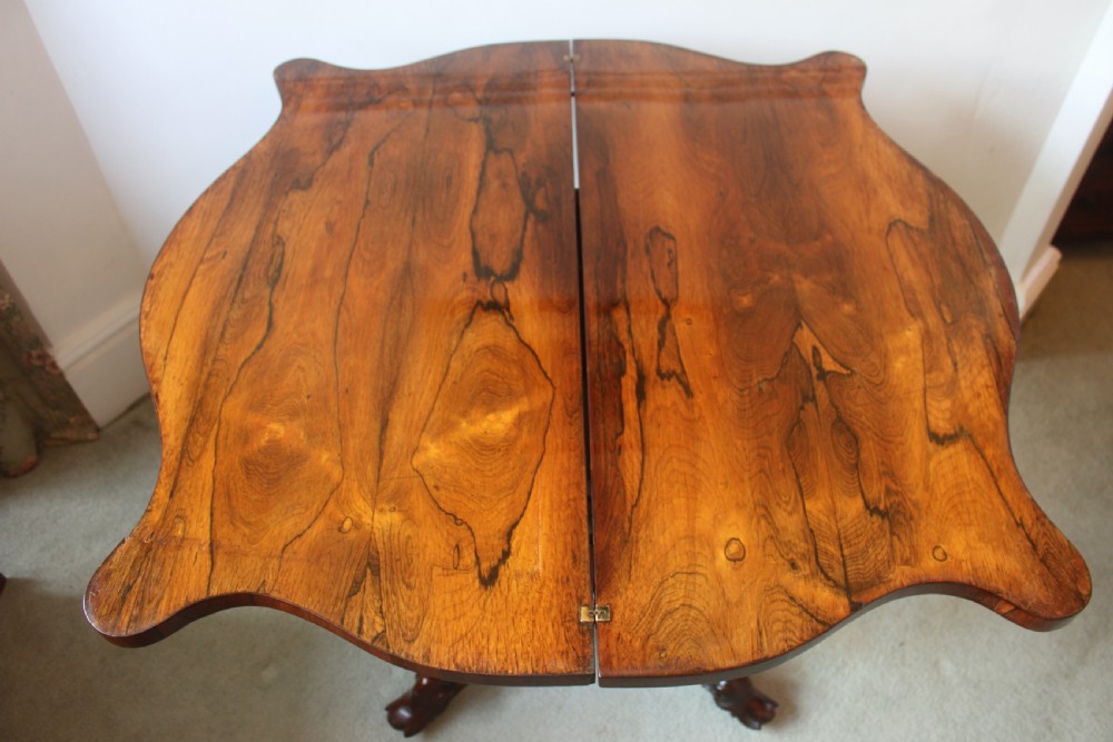 A Victorian rosewood foldover tea table featuring a serpentine front, carved pedestal stem, and quad-form cabriole legs. View XV