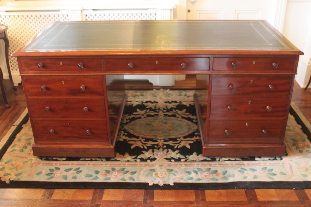An early 19th-century mahogany pedestal desk featuring a dark green leather writing top, nine drawers with turned wooden knobs, and a plinth base.