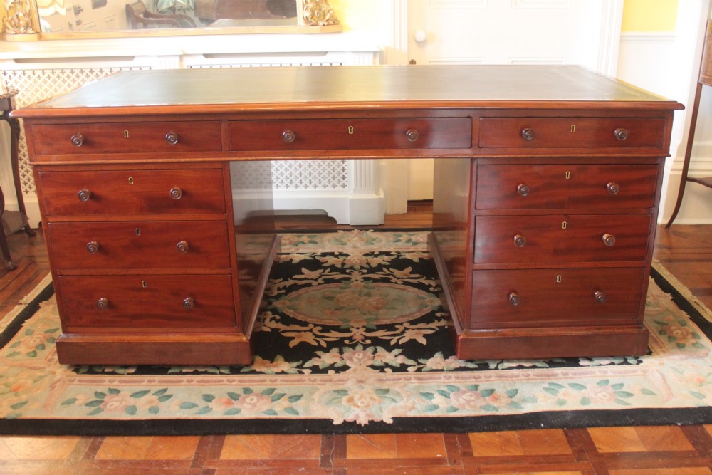 An early 19th-century mahogany pedestal desk featuring a dark green leather writing top, nine drawers with turned wooden knobs, and a plinth base. View II