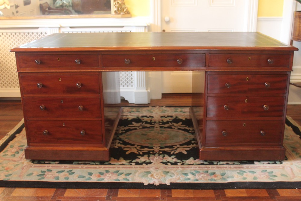 An early 19th-century mahogany pedestal desk featuring a dark green leather writing top, nine drawers with turned wooden knobs, and a plinth base. View III