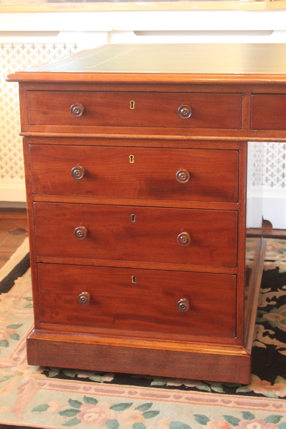 An early 19th-century mahogany pedestal desk featuring a dark green leather writing top, nine drawers with turned wooden knobs, and a plinth base. View V
