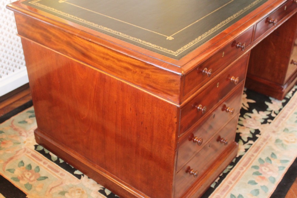 An early 19th-century mahogany pedestal desk featuring a dark green leather writing top, nine drawers with turned wooden knobs, and a plinth base. View VI