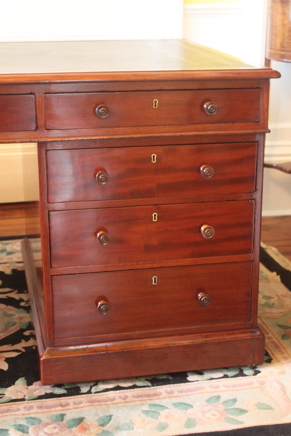 An early 19th-century mahogany pedestal desk featuring a dark green leather writing top, nine drawers with turned wooden knobs, and a plinth base. View VII