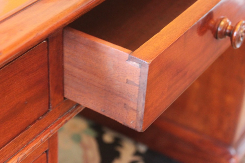 An early 19th-century mahogany pedestal desk featuring a dark green leather writing top, nine drawers with turned wooden knobs, and a plinth base. View IX