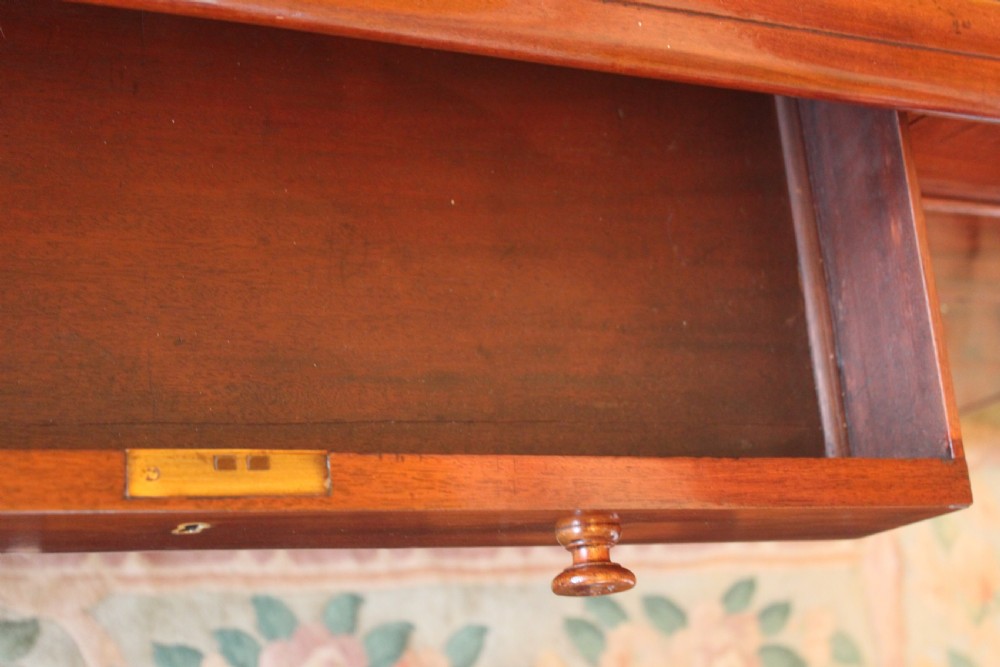 An early 19th-century mahogany pedestal desk featuring a dark green leather writing top, nine drawers with turned wooden knobs, and a plinth base. View X