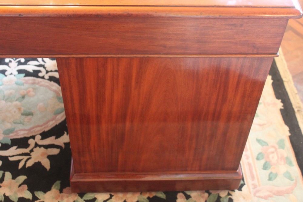 An early 19th-century mahogany pedestal desk featuring a dark green leather writing top, nine drawers with turned wooden knobs, and a plinth base. View XII