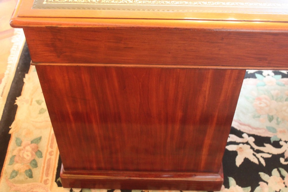An early 19th-century mahogany pedestal desk featuring a dark green leather writing top, nine drawers with turned wooden knobs, and a plinth base. View XIII