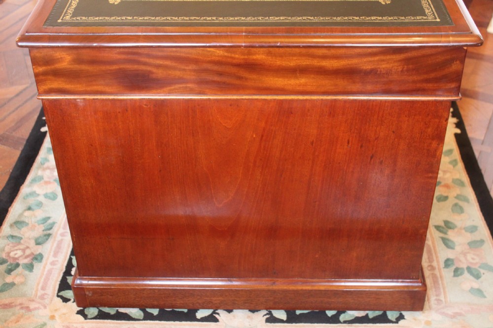 An early 19th-century mahogany pedestal desk featuring a dark green leather writing top, nine drawers with turned wooden knobs, and a plinth base. View XVI