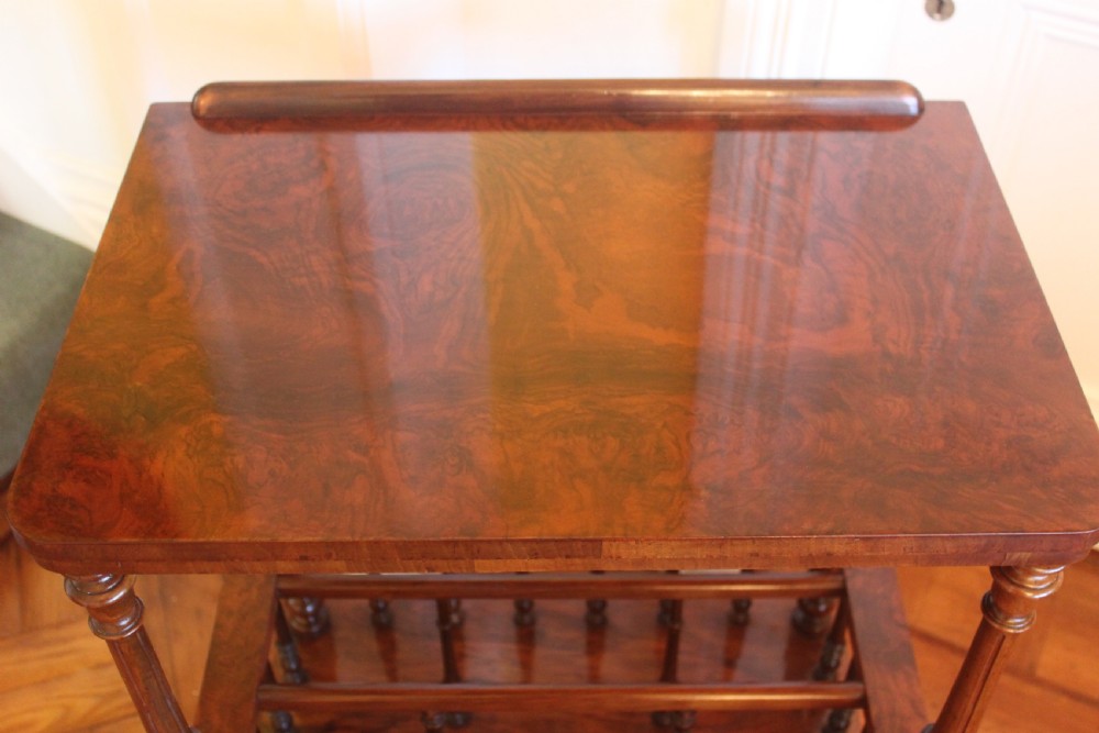 A Victorian burr walnut Canterbury what-not featuring a flat top surface with a gallery rail, turned spindle supports, a slatted middle partition section, a single base drawer, and turned legs with brass castors. View III