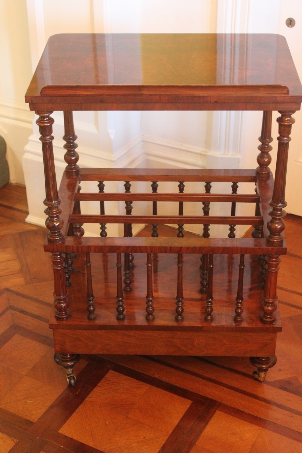 A Victorian burr walnut Canterbury what-not featuring a flat top surface with a gallery rail, turned spindle supports, a slatted middle partition section, a single base drawer, and turned legs with brass castors. View VI