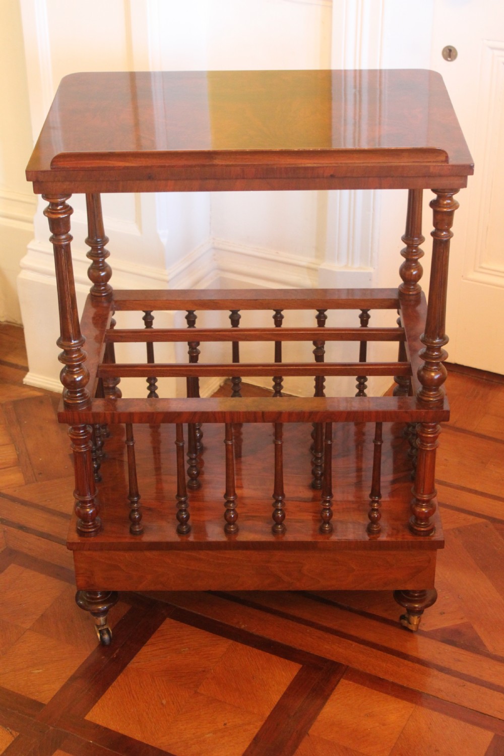 A Victorian burr walnut Canterbury what-not featuring a flat top surface with a gallery rail, turned spindle supports, a slatted middle partition section, a single base drawer, and turned legs with brass castors. View VII