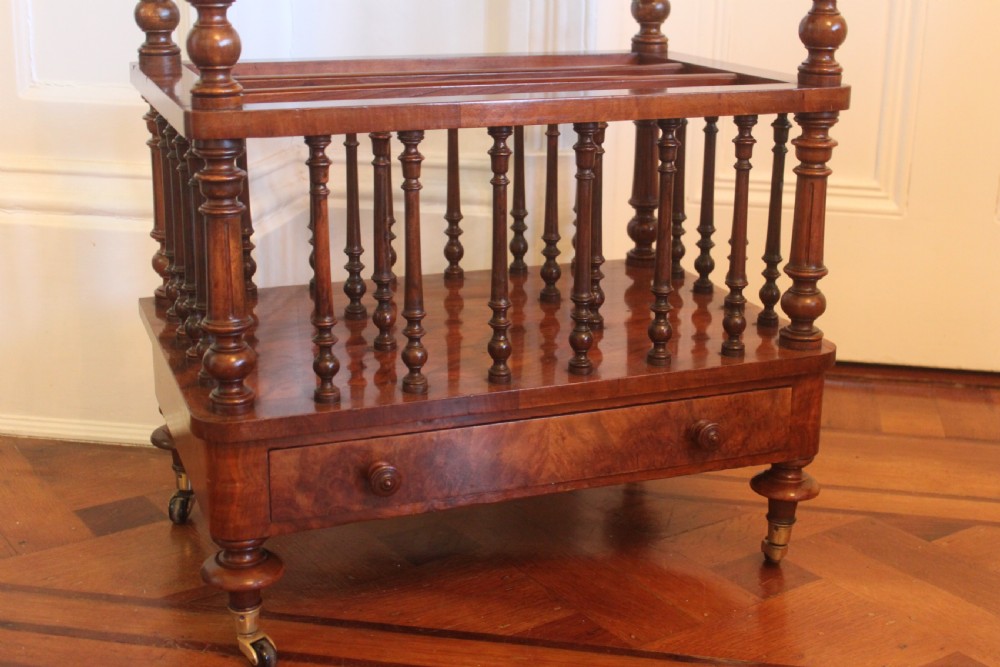 A Victorian burr walnut Canterbury what-not featuring a flat top surface with a gallery rail, turned spindle supports, a slatted middle partition section, a single base drawer, and turned legs with brass castors. View IX