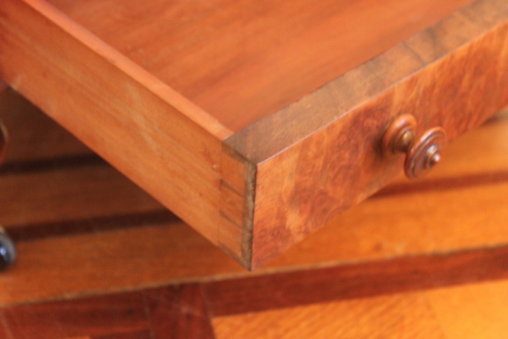 A Victorian burr walnut Canterbury what-not featuring a flat top surface with a gallery rail, turned spindle supports, a slatted middle partition section, a single base drawer, and turned legs with brass castors. View XI