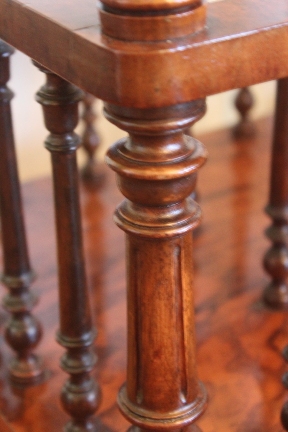A Victorian burr walnut Canterbury what-not featuring a flat top surface with a gallery rail, turned spindle supports, a slatted middle partition section, a single base drawer, and turned legs with brass castors. View XII