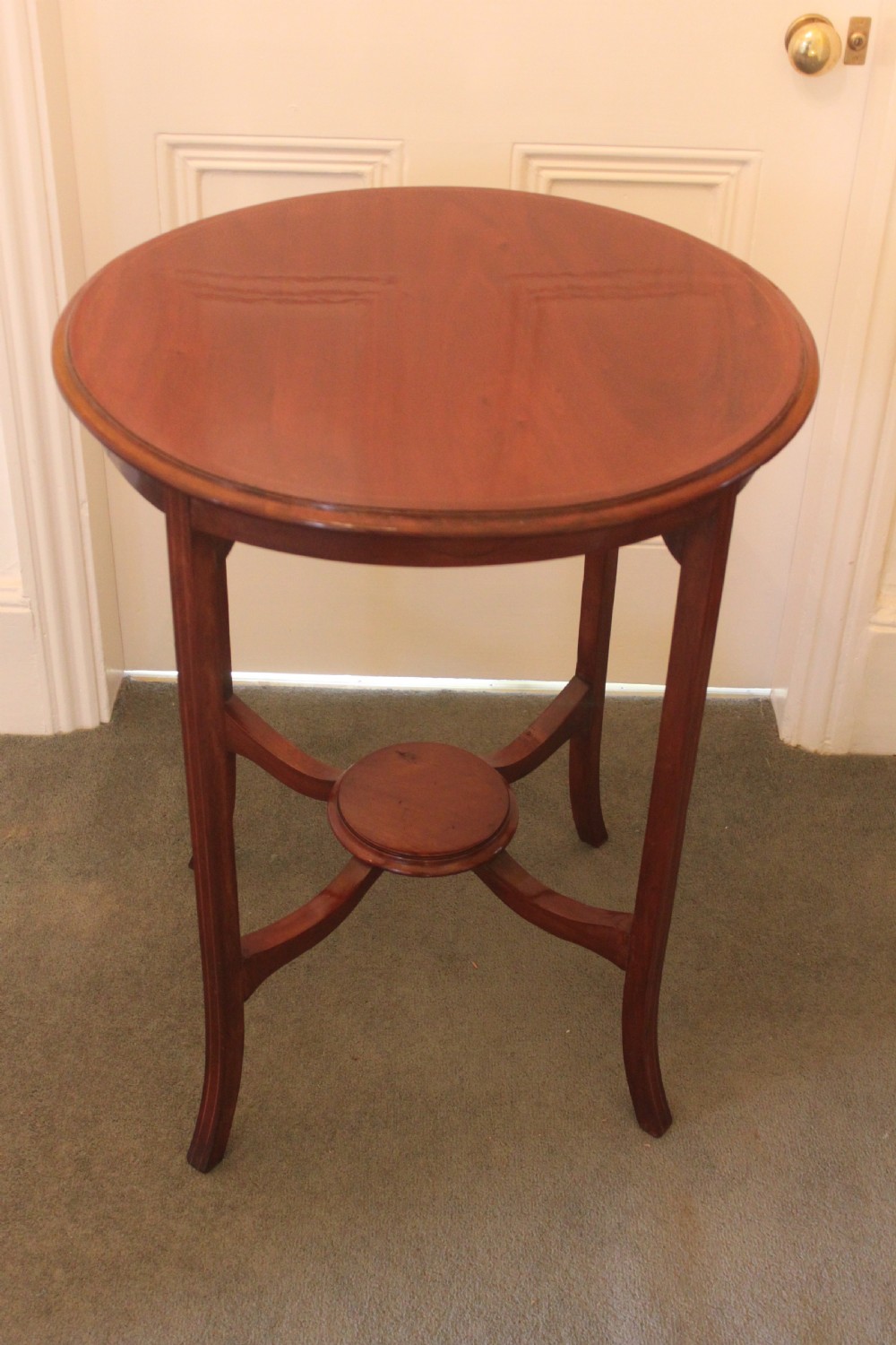 An Edwardian mahogany circular occasional table featuring slender curved legs connected by an X-shaped cross-stretcher with a small circular central under-tier.
