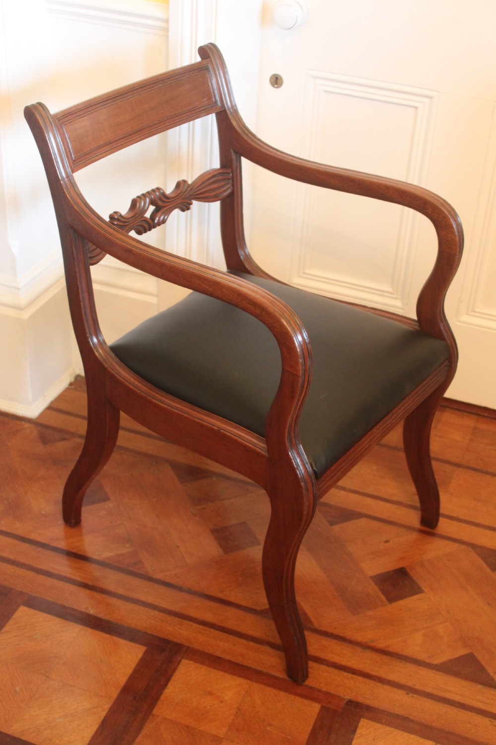 An antique Regency mahogany desk chair featuring sweeping reeded arms, a carved central back rail, and a black leather seat. View II