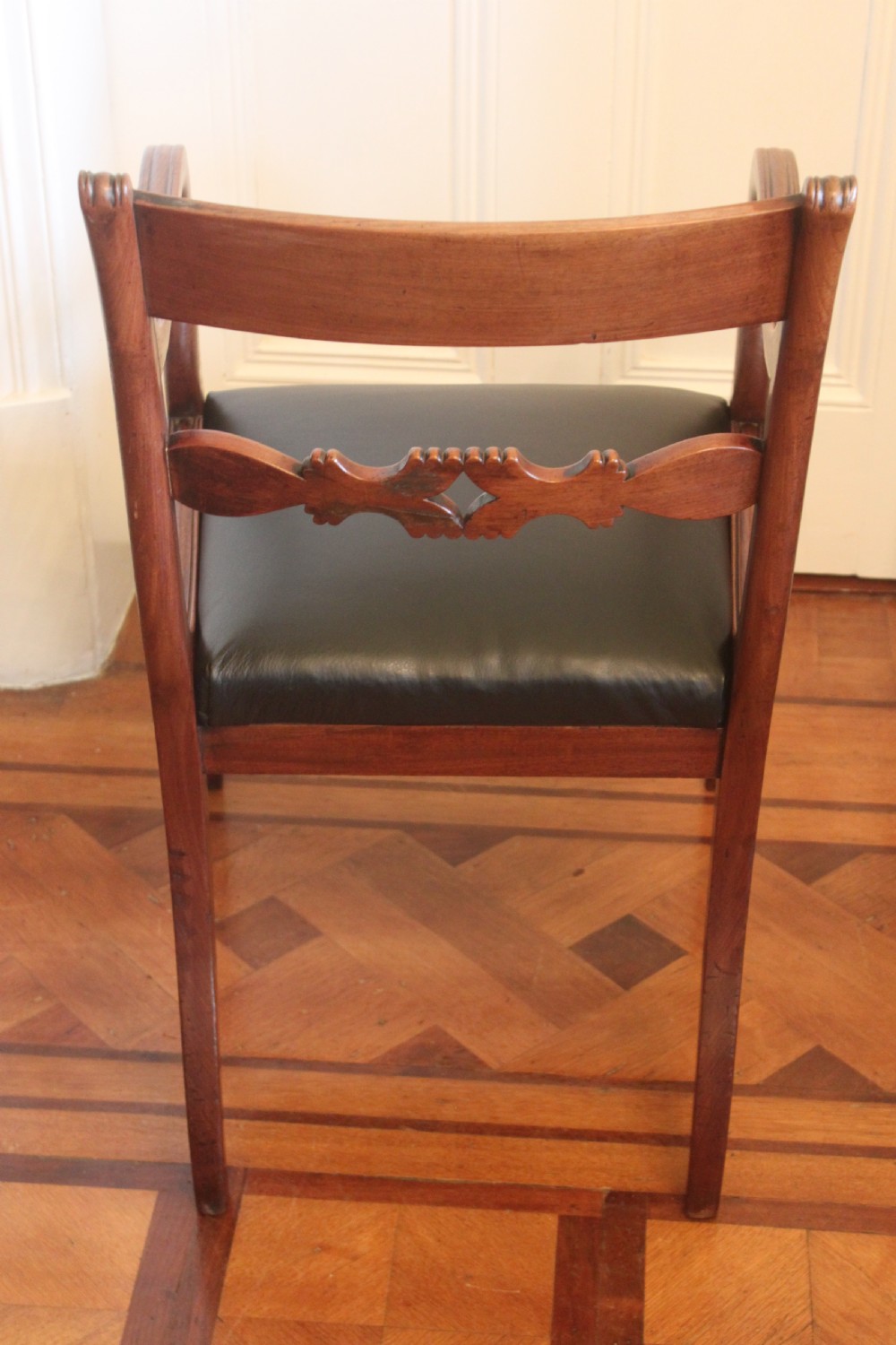 An antique Regency mahogany desk chair featuring sweeping reeded arms, a carved central back rail, and a black leather seat. View III