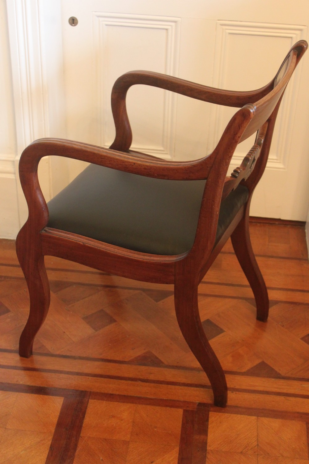 An antique Regency mahogany desk chair featuring sweeping reeded arms, a carved central back rail, and a black leather seat. View IV