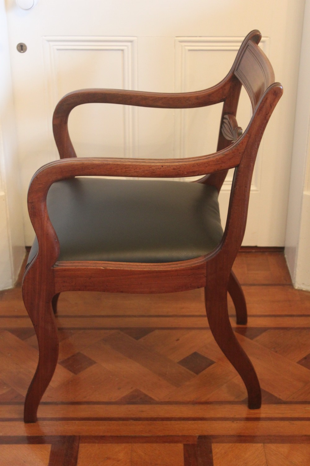 An antique Regency mahogany desk chair featuring sweeping reeded arms, a carved central back rail, and a black leather seat. View V