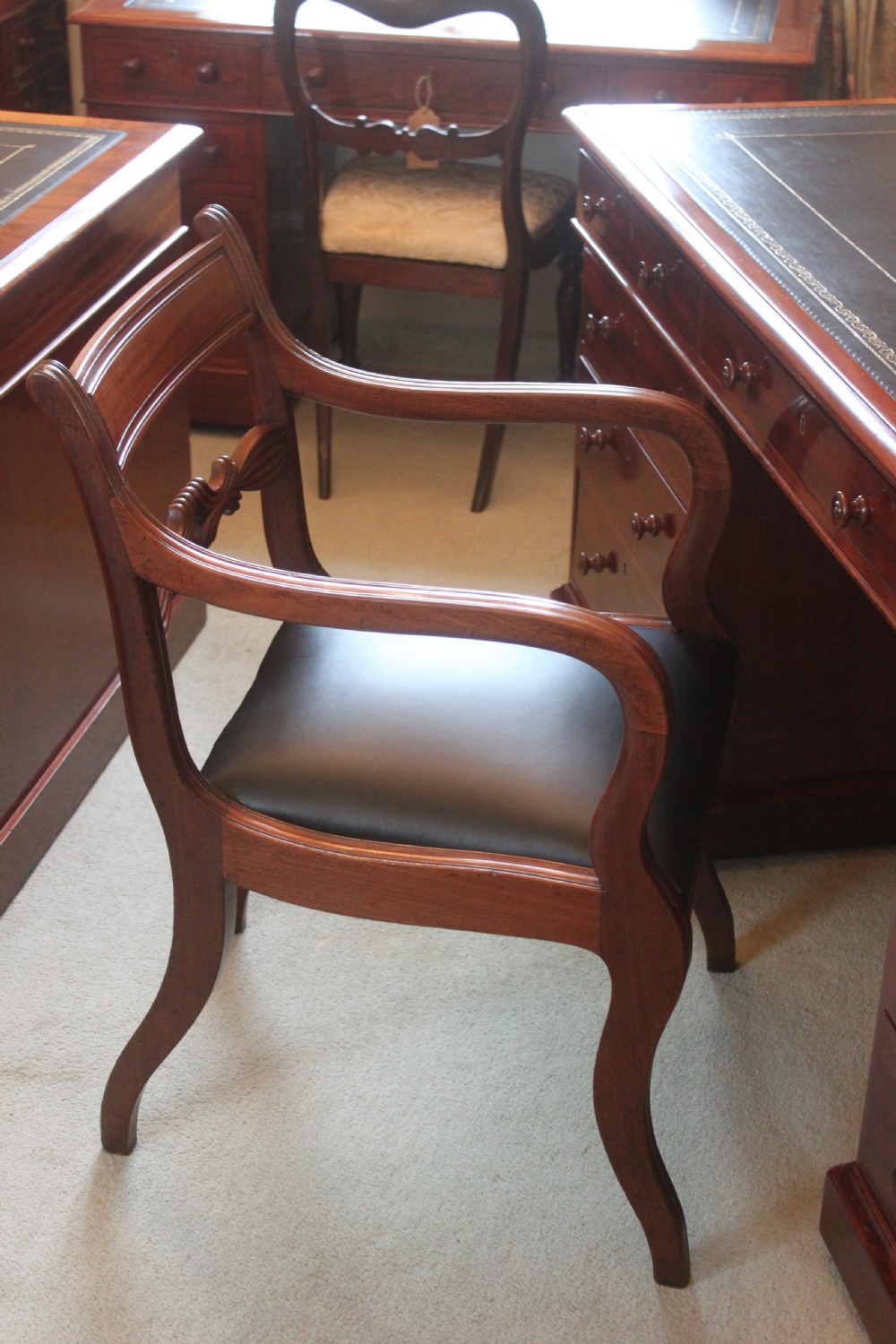 An antique Regency mahogany desk chair featuring sweeping reeded arms, a carved central back rail, and a black leather seat. View X