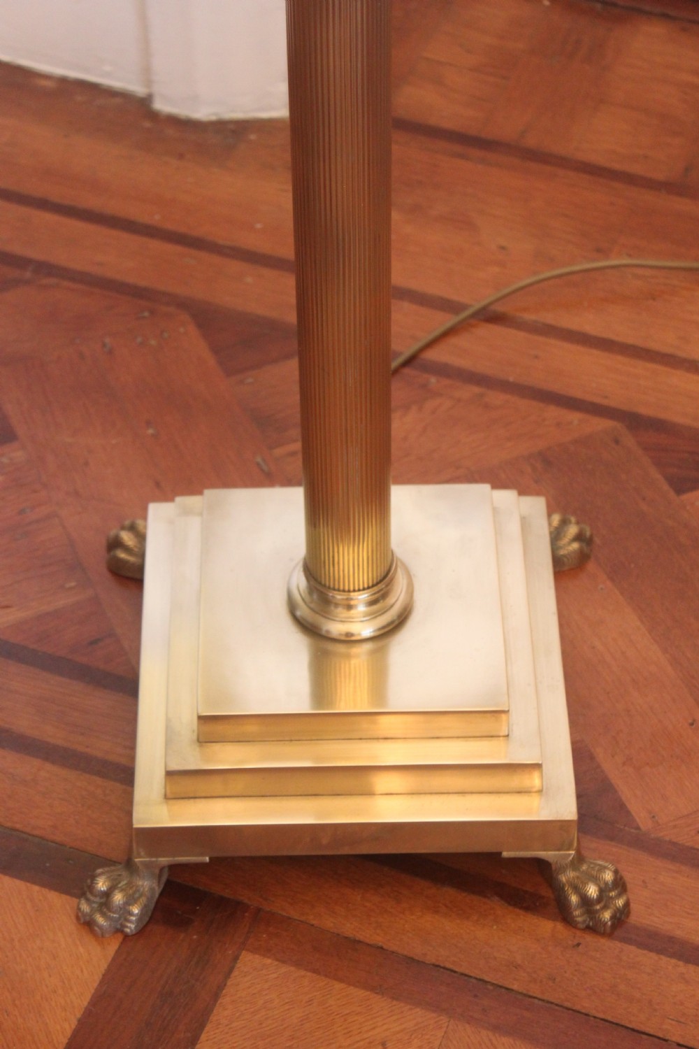 An antique brass standard lamp featuring a fluted column stem, decorative capital, stepped square pedestal base, and a cream pleated shade. View III