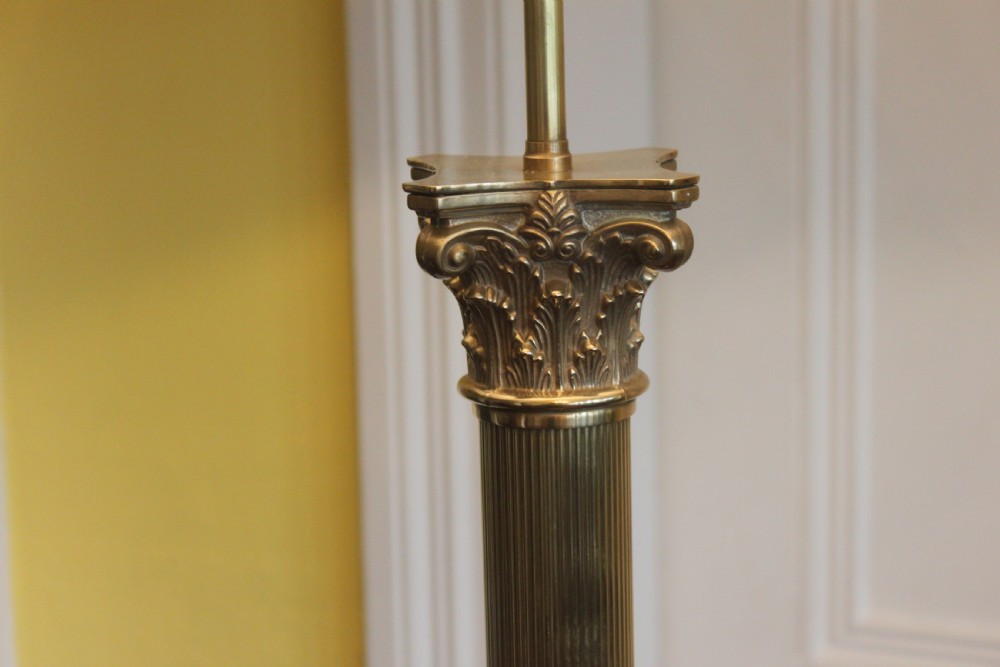 An antique brass standard lamp featuring a fluted column stem, decorative capital, stepped square pedestal base, and a cream pleated shade. View V