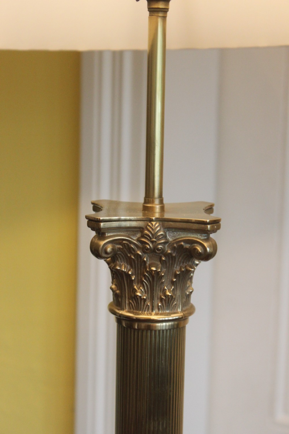 An antique brass standard lamp featuring a fluted column stem, decorative capital, stepped square pedestal base, and a cream pleated shade. View VI