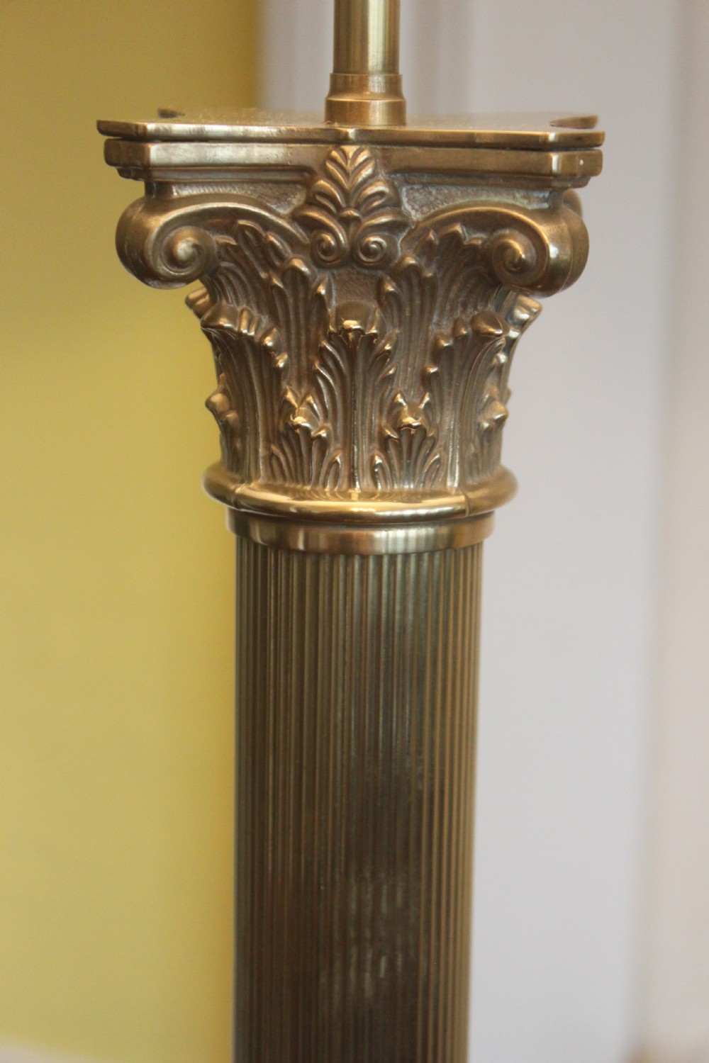 An antique brass standard lamp featuring a fluted column stem, decorative capital, stepped square pedestal base, and a cream pleated shade. View VII