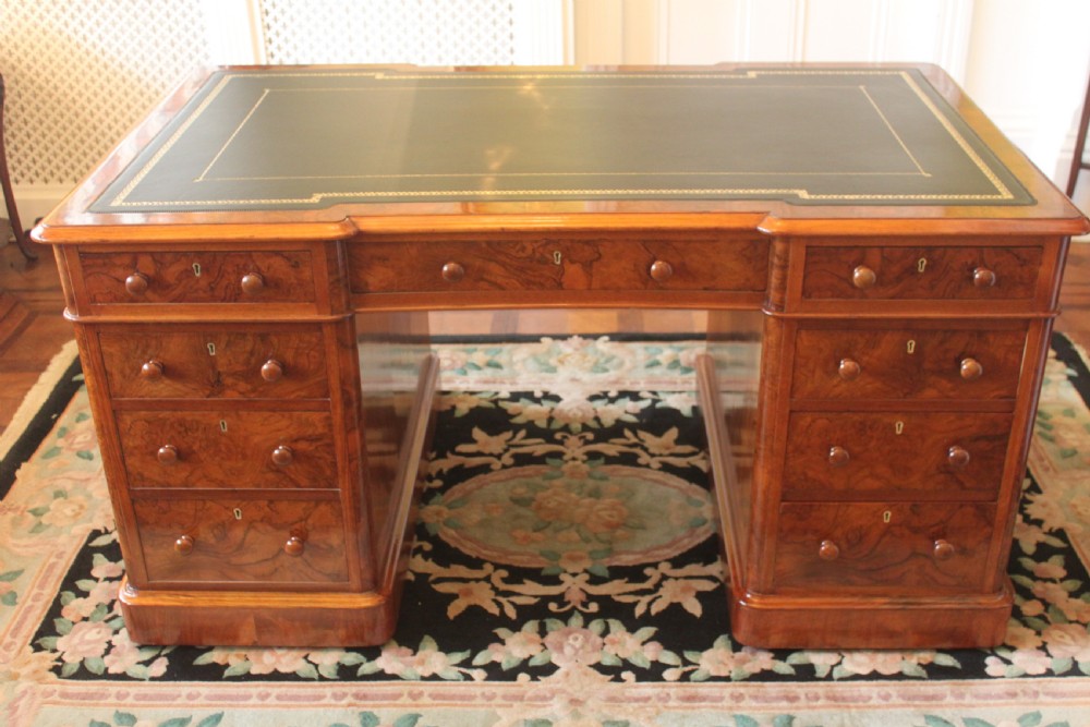 A Victorian burr walnut partners desk with a green leather inset writing top, twin pedestals containing multiple drawers with turned wooden handles, resting on plinth bases.