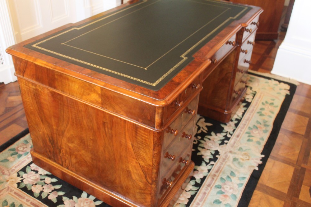 A Victorian burr walnut partners desk with a green leather inset writing top, twin pedestals containing multiple drawers with turned wooden handles, resting on plinth bases. View III
