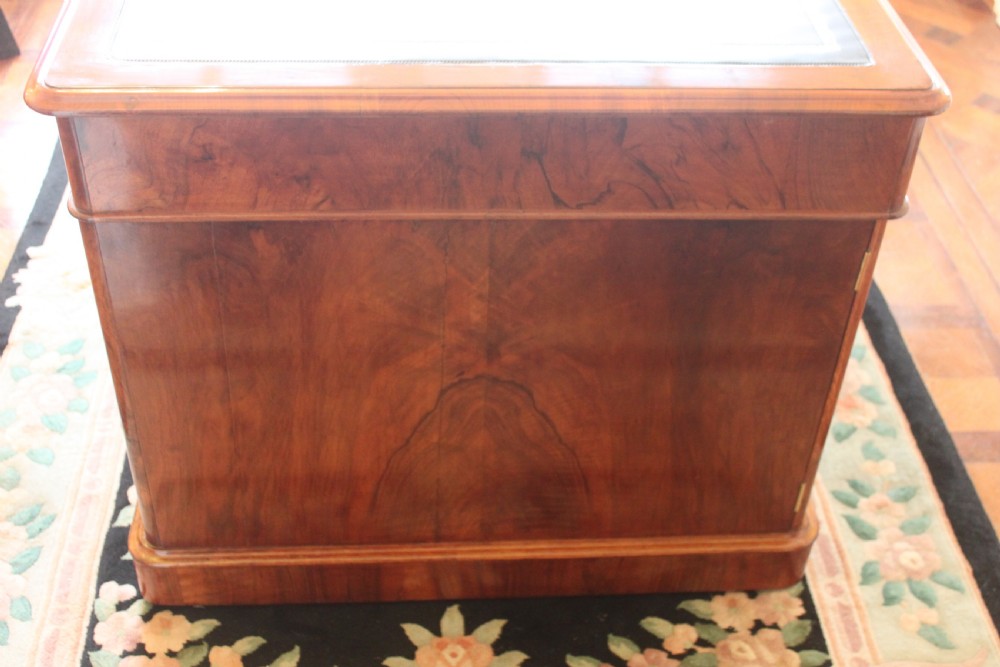 A Victorian burr walnut partners desk with a green leather inset writing top, twin pedestals containing multiple drawers with turned wooden handles, resting on plinth bases. View VI