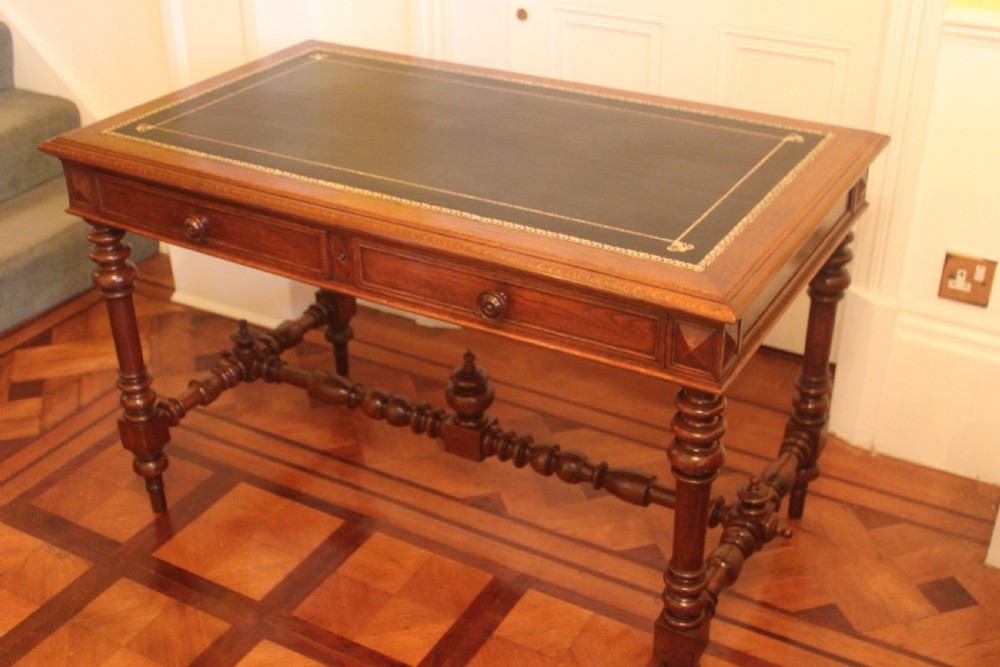 An antique French oak writing desk featuring a gold-tooled dark leather top insert, frieze drawers, turned baluster legs, and a stretcher base with a central finial. View III