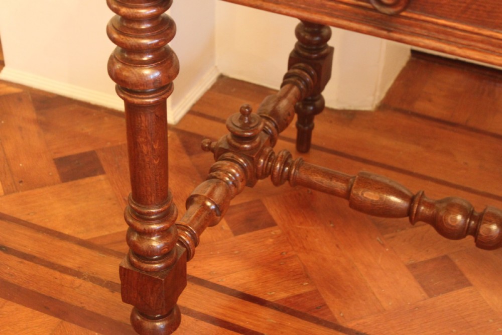 An antique French oak writing desk featuring a gold-tooled dark leather top insert, frieze drawers, turned baluster legs, and a stretcher base with a central finial. View VIII